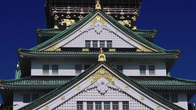 Detail of Osaka Castle in Japan with stunning blue sky behind and birds flying past. The roof is green with beautiful gold detail