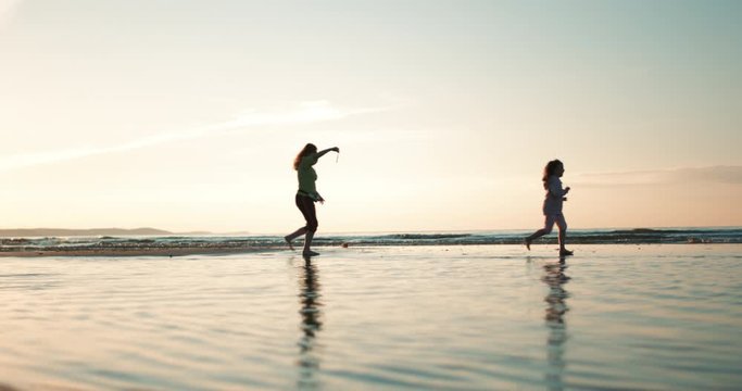 Kobieta z c&oacute;rką biegną po plaży o zachodzie słońca - sylwetki.