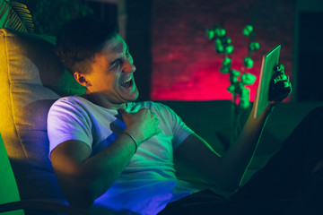 Laughting. Cinematic portrait of stylish man in neon lighted interior. Toned like cinema effects, bright neoned colors. Caucasian model using gadgets, devices in colorful lights indoors. Youth culture