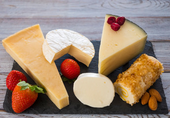 Slices of assorted French, Spanish and Italian cheese on a dark board, served with fruit, wooden background