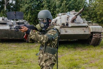 A soldier in a gas mask with a Kalashnikov rifle against the background of armored vehicles.
