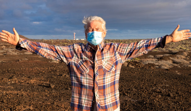 Front view of senior man with medical face mask enjoying nature outdoors. Lighthouse at the horizon. Partial conquest of freedom after coronavirus lockdown - Powered by Adobe