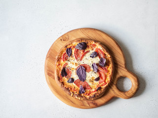 Homemade vegetarian pizza with cheese, tomatoes and purple basil on wooden board. Top view