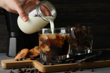 Woman pours a milk in glass of coffee. Composition with ice coffee