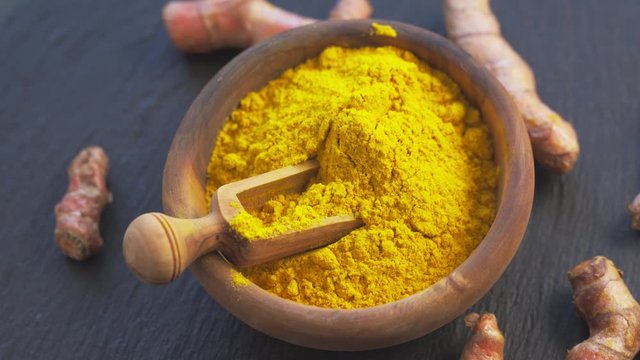 Turmeric powder and roots in wooden bowl rotation