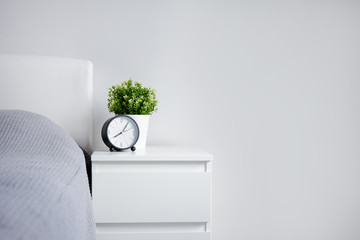 good morning concept - alarm clock and houseplant on bedside table and copy space over white wall