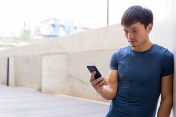 Portrait of young Asian man using phone in the city outdoors