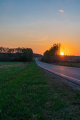 Obraz premium Picturesque rural landscape showing bright orange sunset over the road in the forest in spring