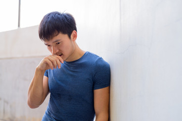 Portrait of young Asian man thinking against the wall outdoors