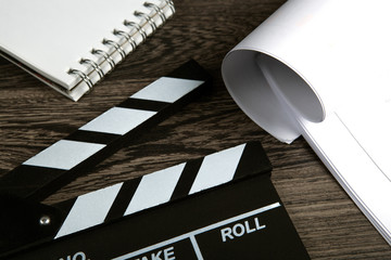 black movie clapper with script sheets and notebook on a wooden table