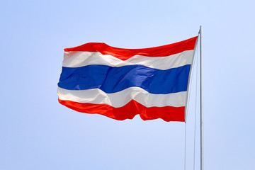 The flag of Thailand against the blue sky flutters in the wind.