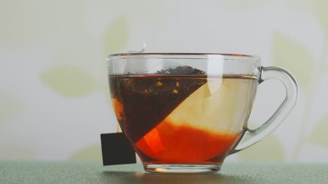 tea bag is brewed in transparent cup timelapse. tea leaves stains water in glass mug closeup.