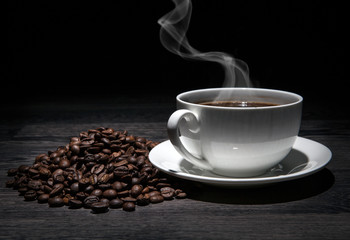 cup of hot coffee and roasted coffee beans on a wooden table on a black background