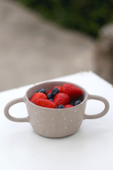 Bowl of blueberries and strawberries on a table in a yard. Selective focus.