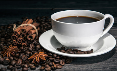 cup of hot coffee and roasted coffee beans with cinnamon sticks on a wooden table