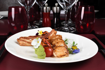 Scallops, bacon, pear and mint puree served on a white plate in a restaurant setting.