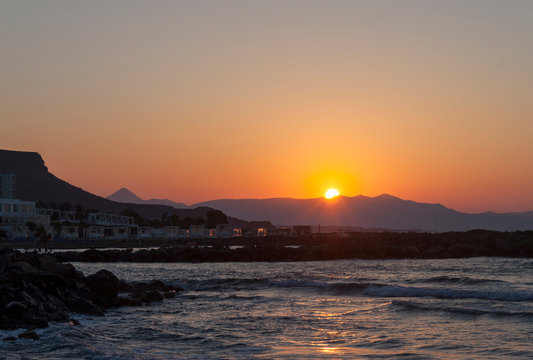 Sunset over the sea in Kokkini Hani, Crete, Greece.  The sun disappears behind the mountain. Scenic seaside landscape in the evening.