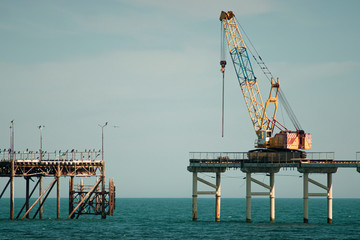 Crane building a fishing pier in turqoise water and demolishing the old one