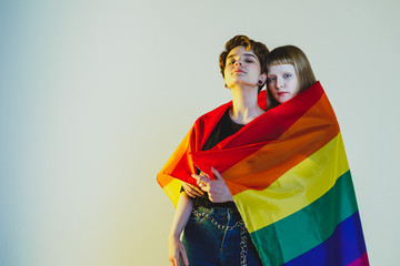 Two beautiful girls lesbians wrapped in a rainbow flag and stand on a white background