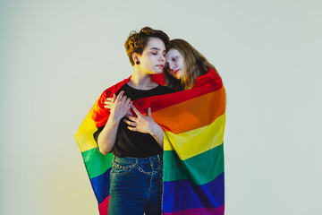 Two beautiful girls lesbians wrapped in a rainbow flag and stand on a white background
