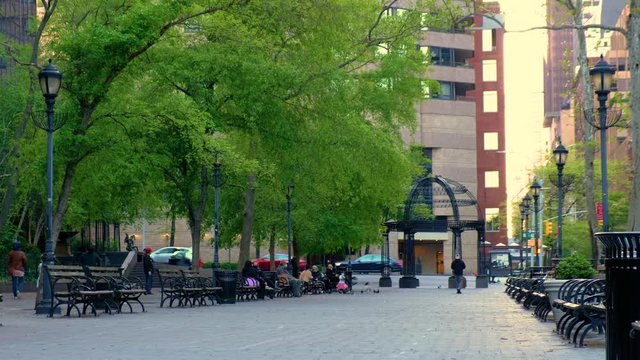 City street park lined with benches and people relaxing.