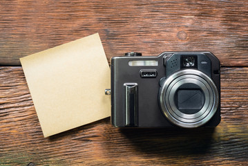 Blank paper sheet and photo camera on wooden table background. Photo list.