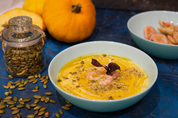 Autumn food - pumpkin soup with cream, shrimps and seeds in bowls on table. Served for dinner. View from above