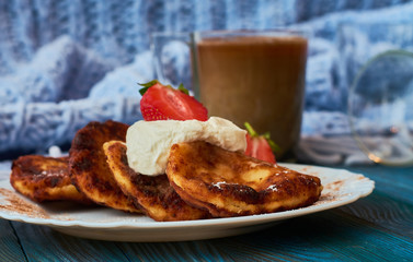 Delicious and useful breakfast of cheese pancakes with sour cream and strawberries cooked at home, with strong black coffee on blue background of wood and plaid.