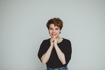 A girl with short hair stands on a white background and smiles