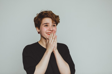 A girl with short hair stands on a white background and smiles