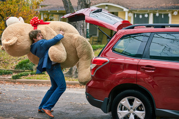 A goofy young man struggling to pull out an oversized teddy bear, stumbling over himself.