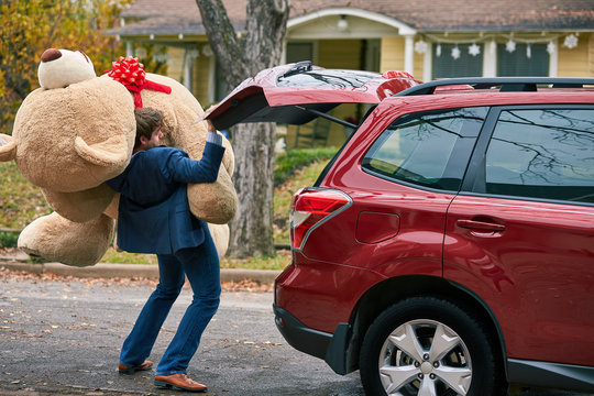 A goofy young man struggling to pull out an oversized teddy bear, stumbling over himself.