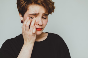 Girl with short hair cries on a white background