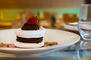 Meringue cake with dark chocolate and strawberry on top, in arestaurant setting, blurred background