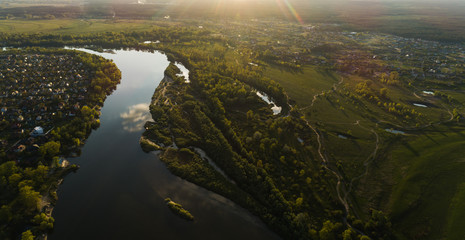 Panoramic aerial view of the nature landscape with green meadows and a river at sunset.