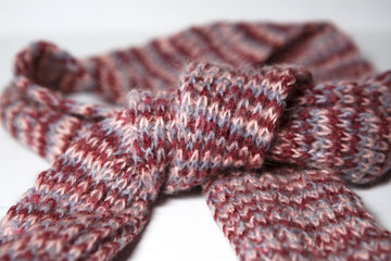 A scarf with round POM-poms made of pink and purple woolen threads of melange color is tied in a knot.