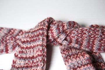 A scarf with round POM-poms made of pink and purple woolen threads of melange color is tied in a knot.