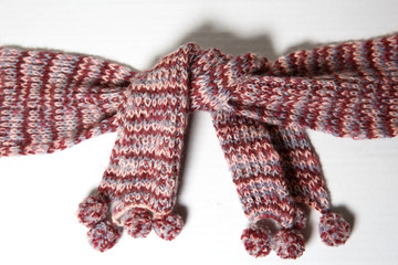 A scarf with round POM-poms made of pink and purple woolen threads of melange color is tied in a knot.