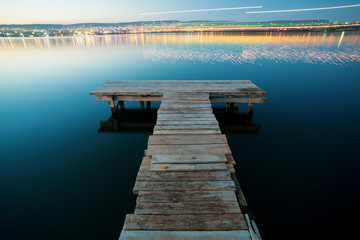 Fototapeta premium Empty Fishing pier at night with the city in the background with orange and teal