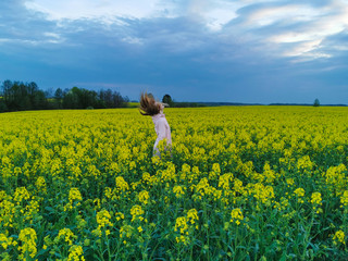 Fototapeta premium Beautiful blonde girl in a rape field before the storm. Girl and flowers.