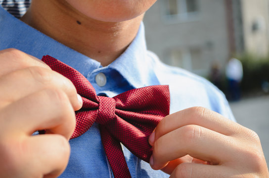 The young man adjusts his red bow tie.
