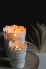 Two candle holders with lit candles and open book on a table. Selective focus, dark and cosy atmosphere.