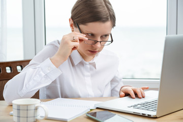 Woman in glasses look through them into computer monitor, looks confused, analyzing economic situation in company.