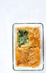 Concetto di cibo greco. Spanakopita, torta greca della pasta fillo con spinaci e feta su un vassoio, sfondo bianco. Vista dall'alto.