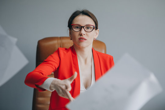 Stressed Woman Sitting At Desk In A Little Office Or Home Mad At Work, Ripping Documents With Frustrated Facial Expression. Throwing Around Scraps Of Paper. Negative Human Emotions