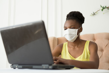 beautiful young african woman sitting in a chair with a laptop in a medical mask