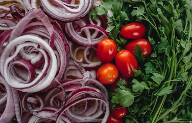 Green parsley on a wooden board, red onion rings and cherry tomatoes, close up. Proper nutrition. Flat lay