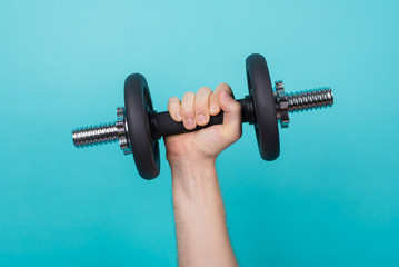 Fototapeta na wymiar Working out concept. Cropped photo of a strong man holding dumbbell in hand isolated on blue background