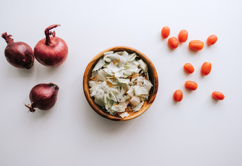 Healthy vegetable salad in a wooden bowl with ingredients on a white table.