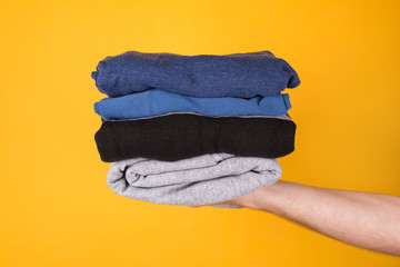 Cropped photo of a man holding stack of folded clothes isolated on yellow background